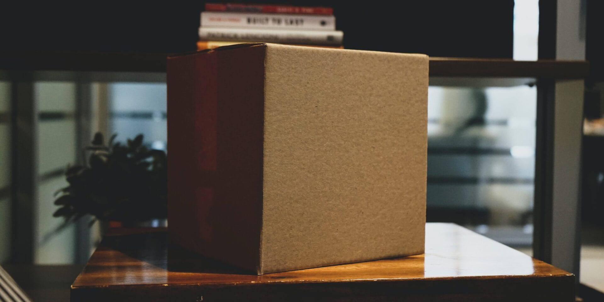 A corrugated box is taped closed and sits atop a desk in a darkened room.