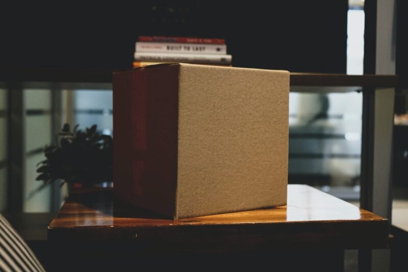 A corrugated box is taped closed and sits atop a desk in a darkened room.