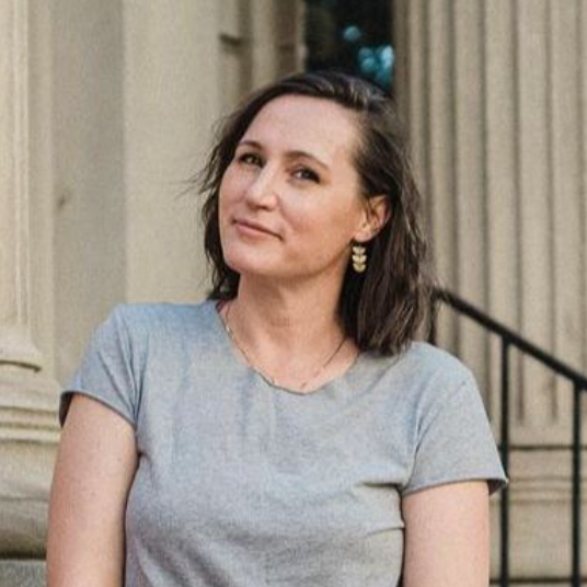 A white woman with shoulder length brown hair in a bust-shot. She is wearing a gray t-shirt.